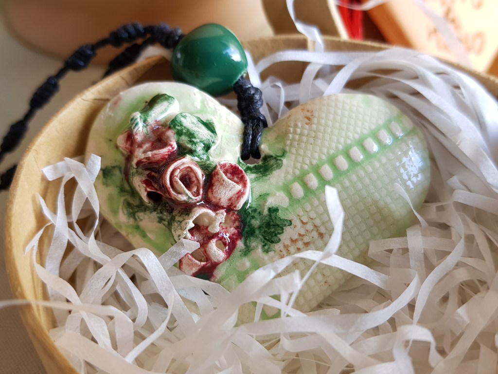 Questo ciondolo a forma di cuore ha una superficie come un merletto verde su cui sono applicate alcune roselline rosa, e delle foglie verdi. Ti sembrerà di sentire il profumo dei fiori di Sicilia!